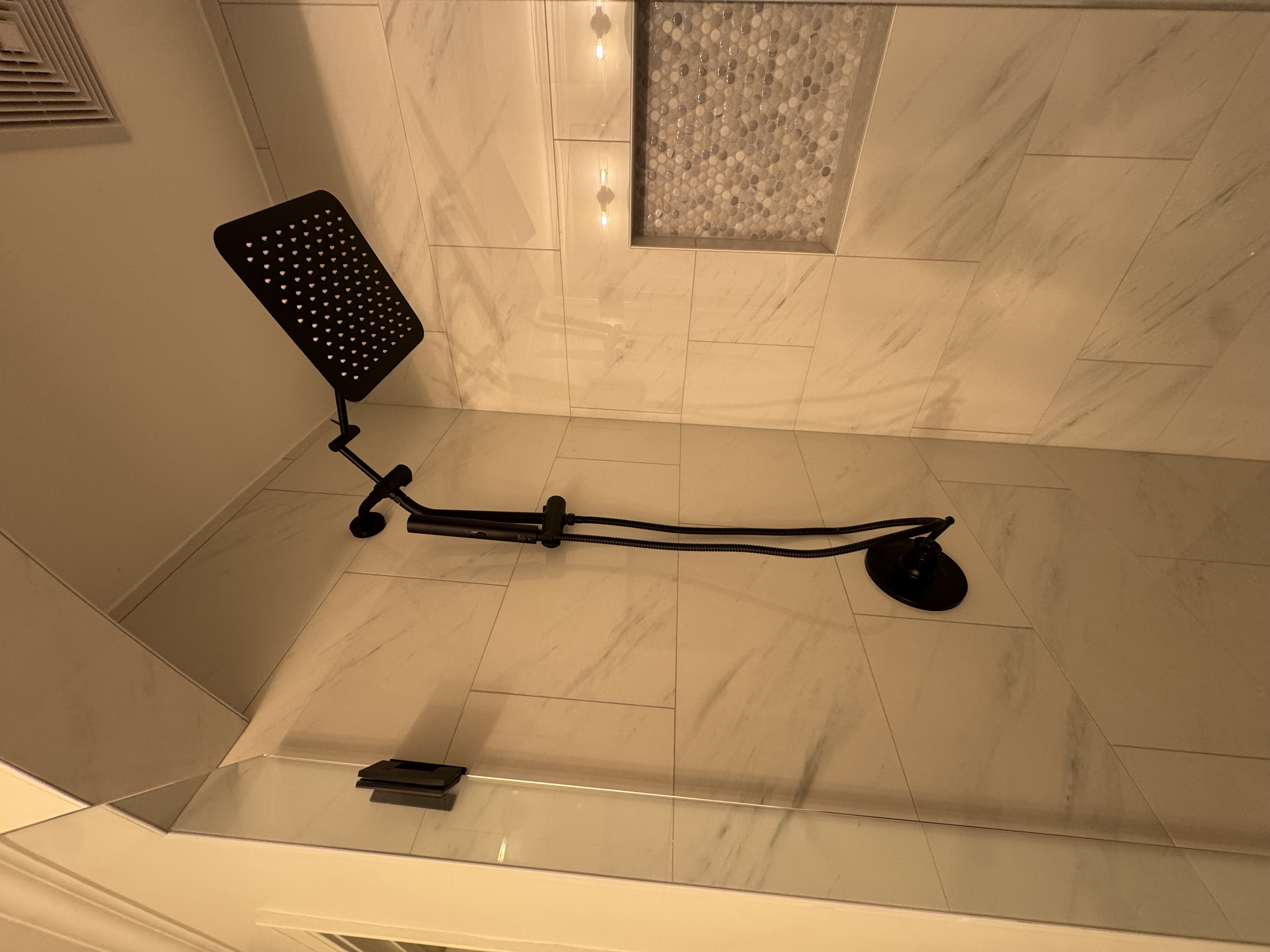 Elegant marble shower with black fixtures and mosaic niche